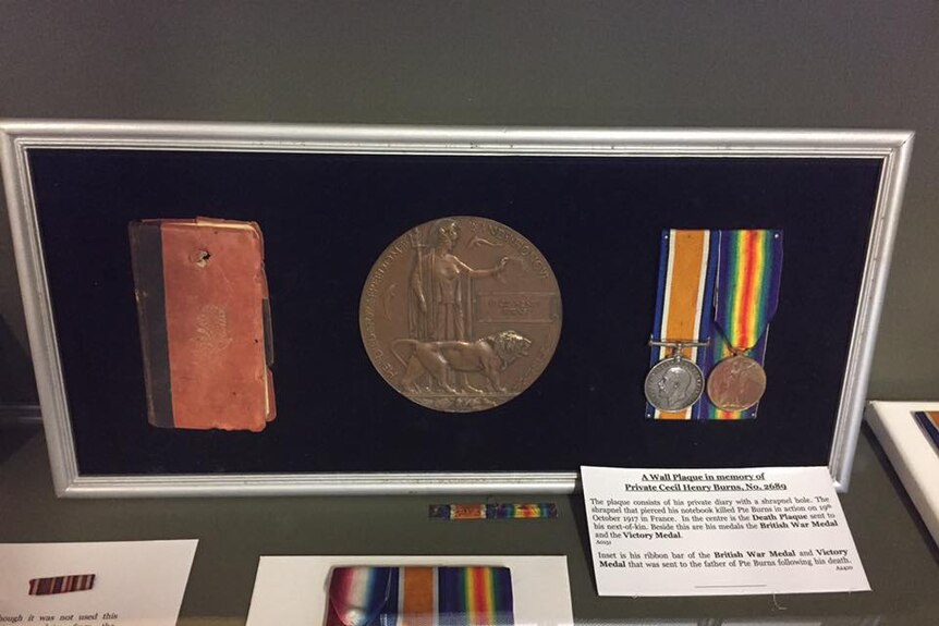 A wall plaque containing Private Cecil Henry Burns' shrapnel pierced diary, his death plaque, and two war medals