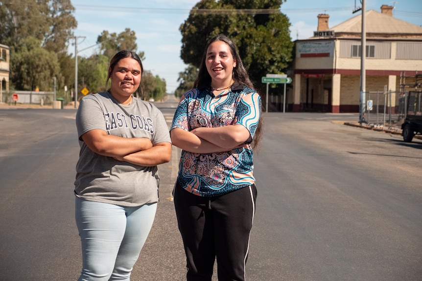 Two women stand with their arms crossed in the middle of the street 