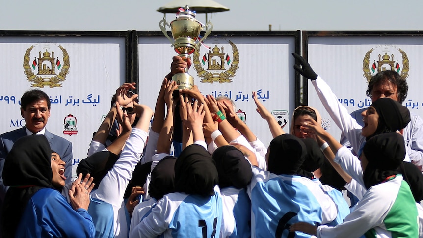 Female football players hold up a trophy.