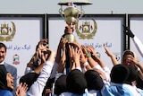 Female football players hold up a trophy.