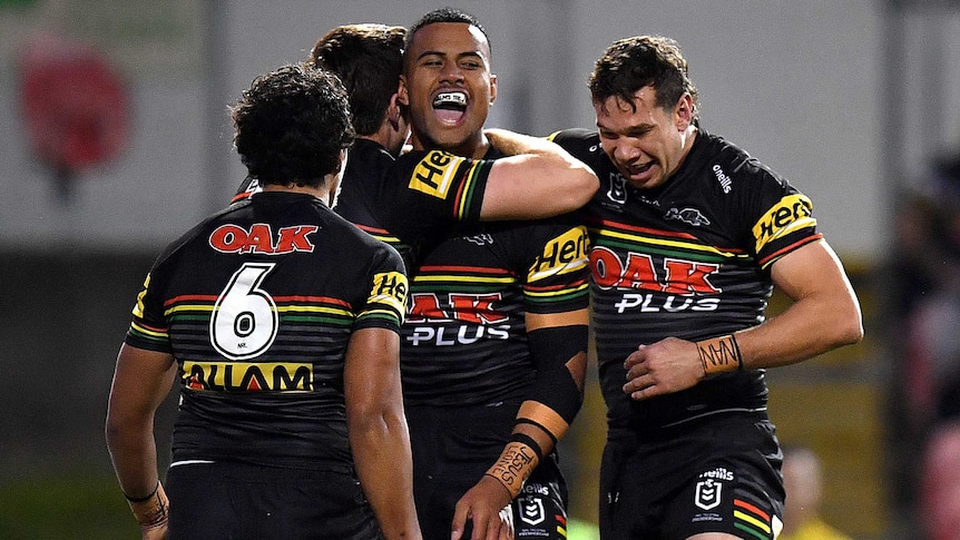 An NRL player shouts in celebration as he is hugged by teammates after a try.