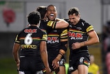 An NRL player shouts in celebration as he is hugged by teammates after a try.