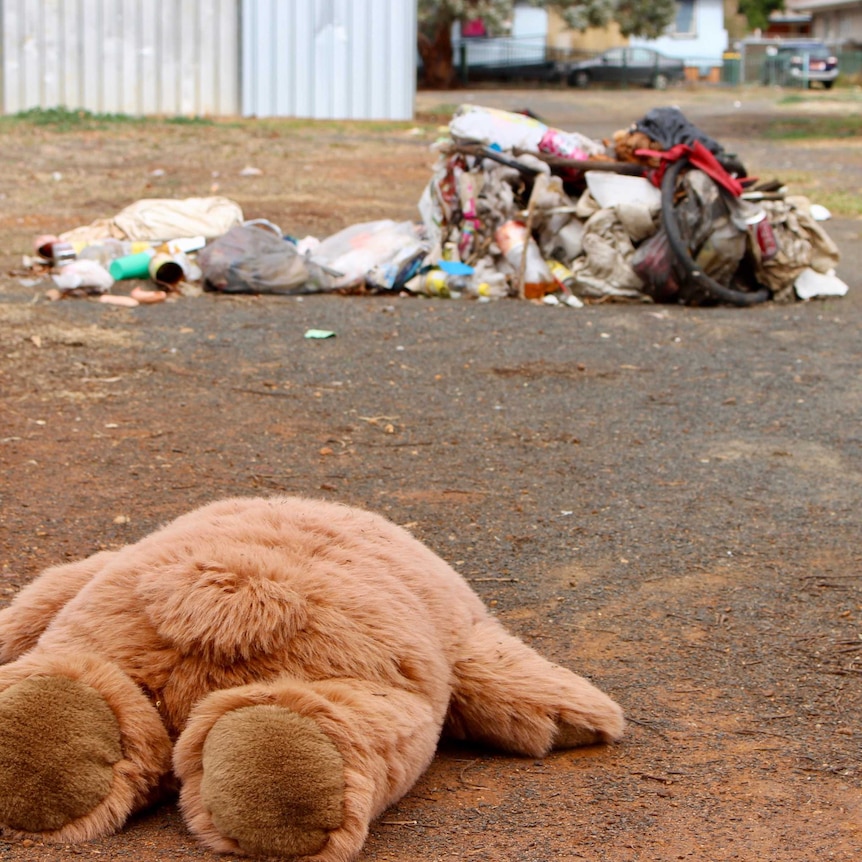 A teddy bear lies face down in front of a pile of garbage in a regional town.