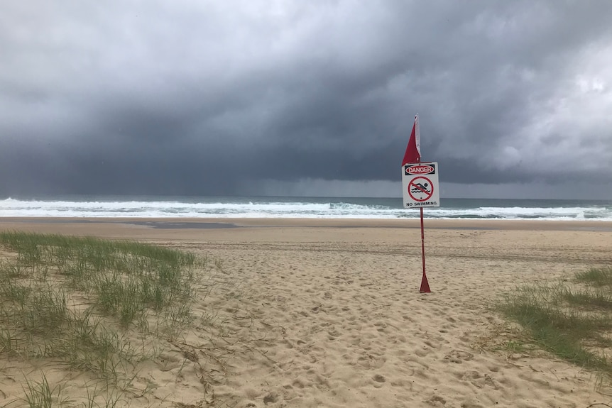 A 'beach closed' sign on Miami beach, with dark storm clouds in background.