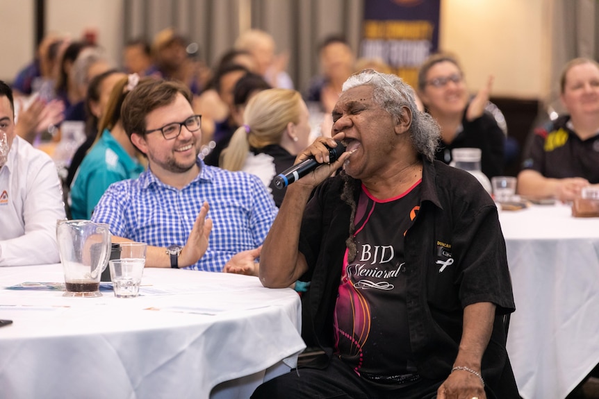 An image of Uncle Robert Bimbo Duncan at a table speaking into a microphone