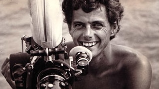 A black and white image of a young man behind a large video camera in the 1970s.