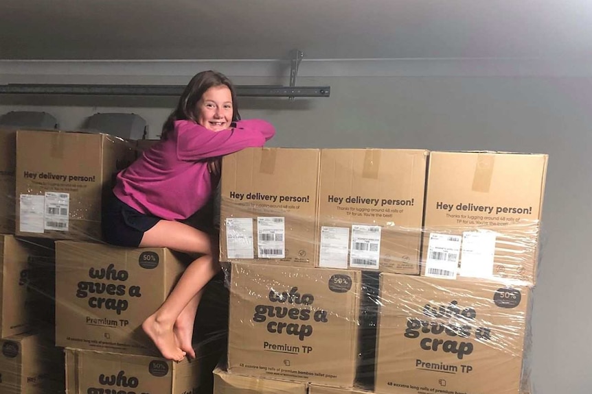 A woman sits on top of two pallets of boxed toilet paper