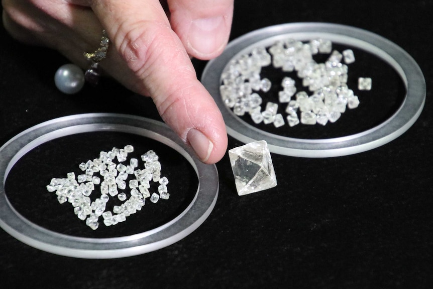 A large cube-shaped diamond on a table next to piles of much smaller diamonds.