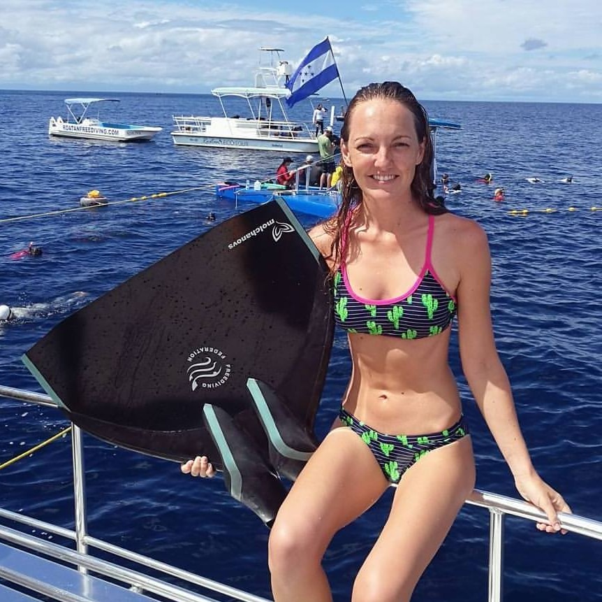 Amber Bourke sitting on the railing of a boat deck in a bikini with a cactus print.