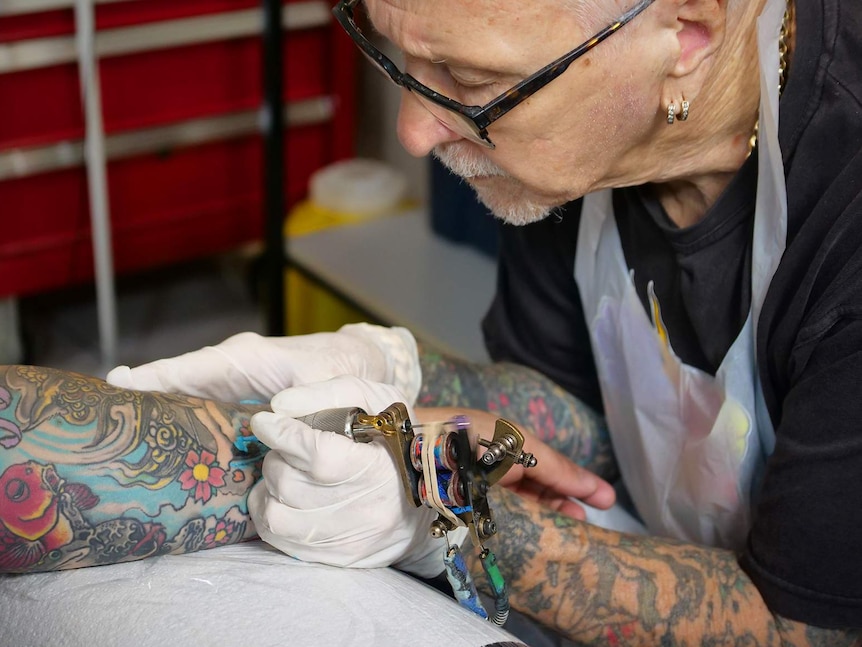 Tattoo artist Les Bowen looks intently while working on a man's tattooed arm in his studio