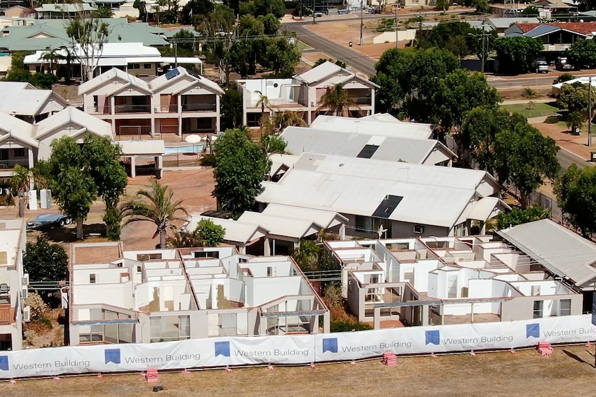 A fence in front of three single storey buildings with no roofs or windows. Double storey units behind are intact.