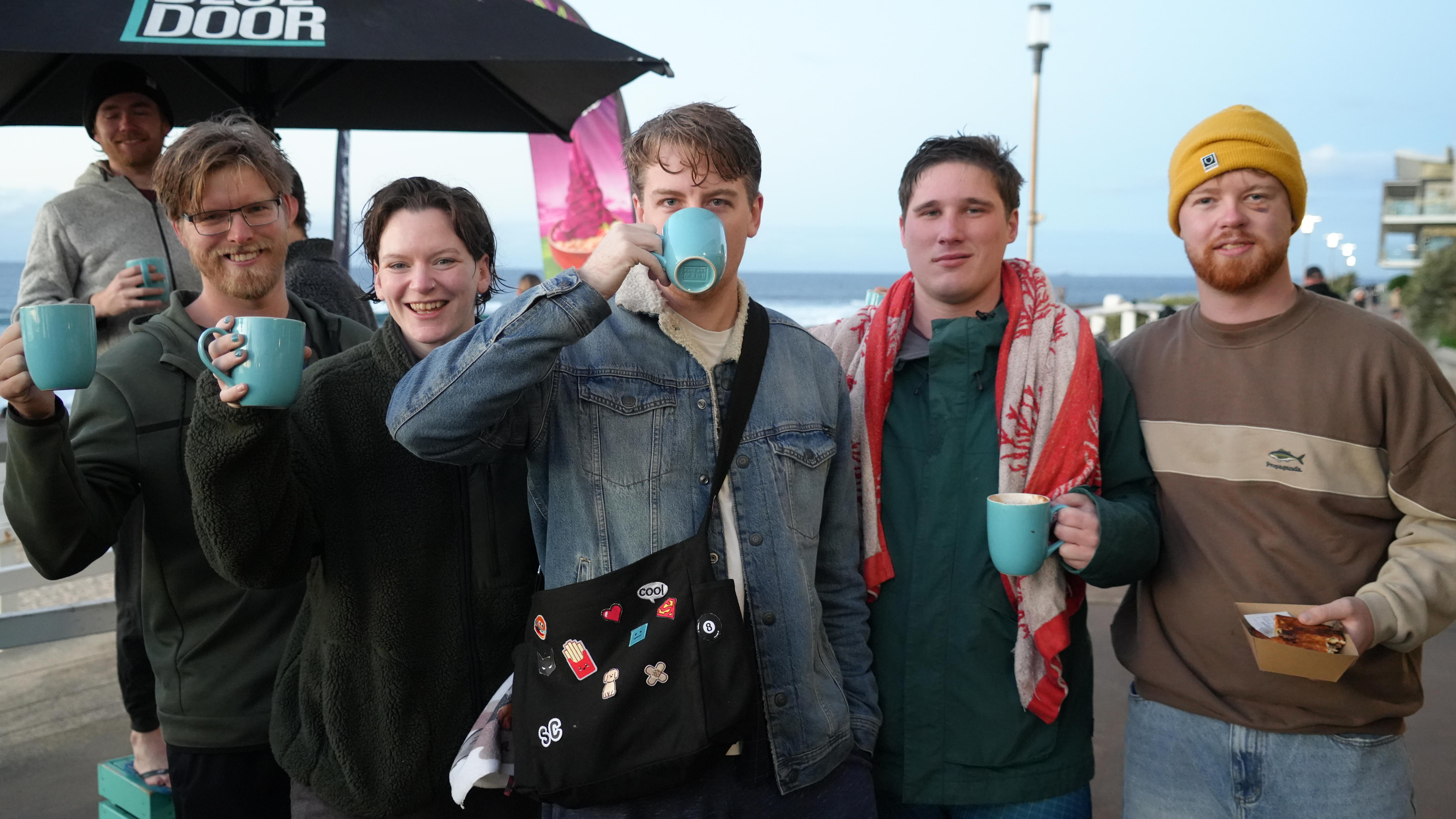 Five people stand smiling, holding coffee cups