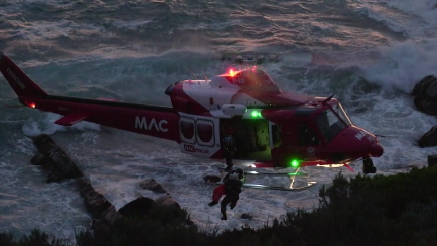 A helicopter hovering above the sea as a man is rescued from a cliff face