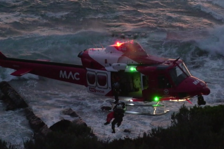 A helicopter hovering above the sea as a man is rescued from a cliff face