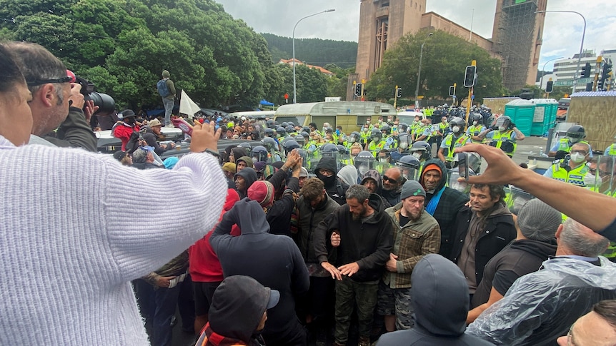 Police with clear shields in high-vis vests surround a crowd made up mainly of middle-aged men dressed in civilian garb 