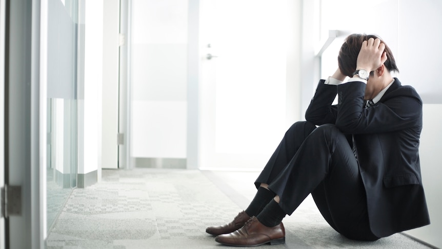 man in suit sitting on floor in modern office building, head in hands
