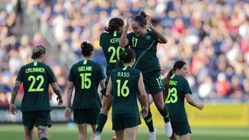 Sam kerr and Kyah Simon jump into each other side on to celebrate with teammates around them