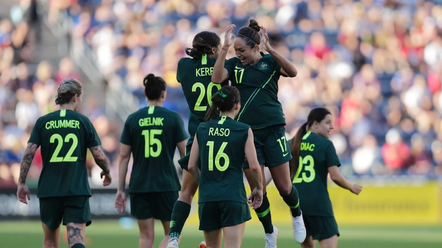 Sam kerr and Kyah Simon jump into each other side on to celebrate with teammates around them
