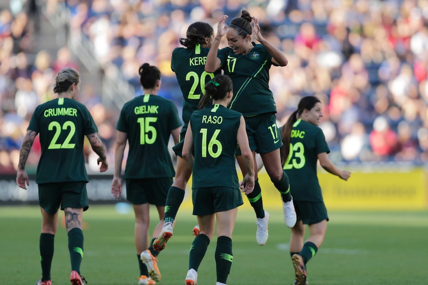 Sam kerr and Kyah Simon jump into each other side on to celebrate with teammates around them