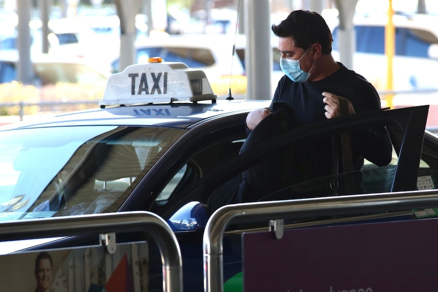 A man gets into a taxi on the way to quarantine after getting off a flight from Melbourne.