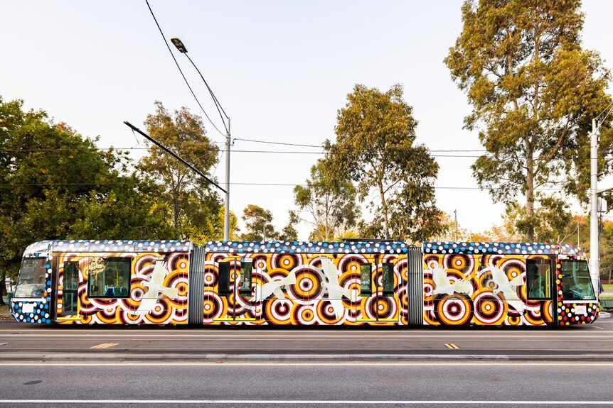 A tram in Melbourne, painted with a bright circular pattern, with white birds, in the style of Indigenous Australian artists