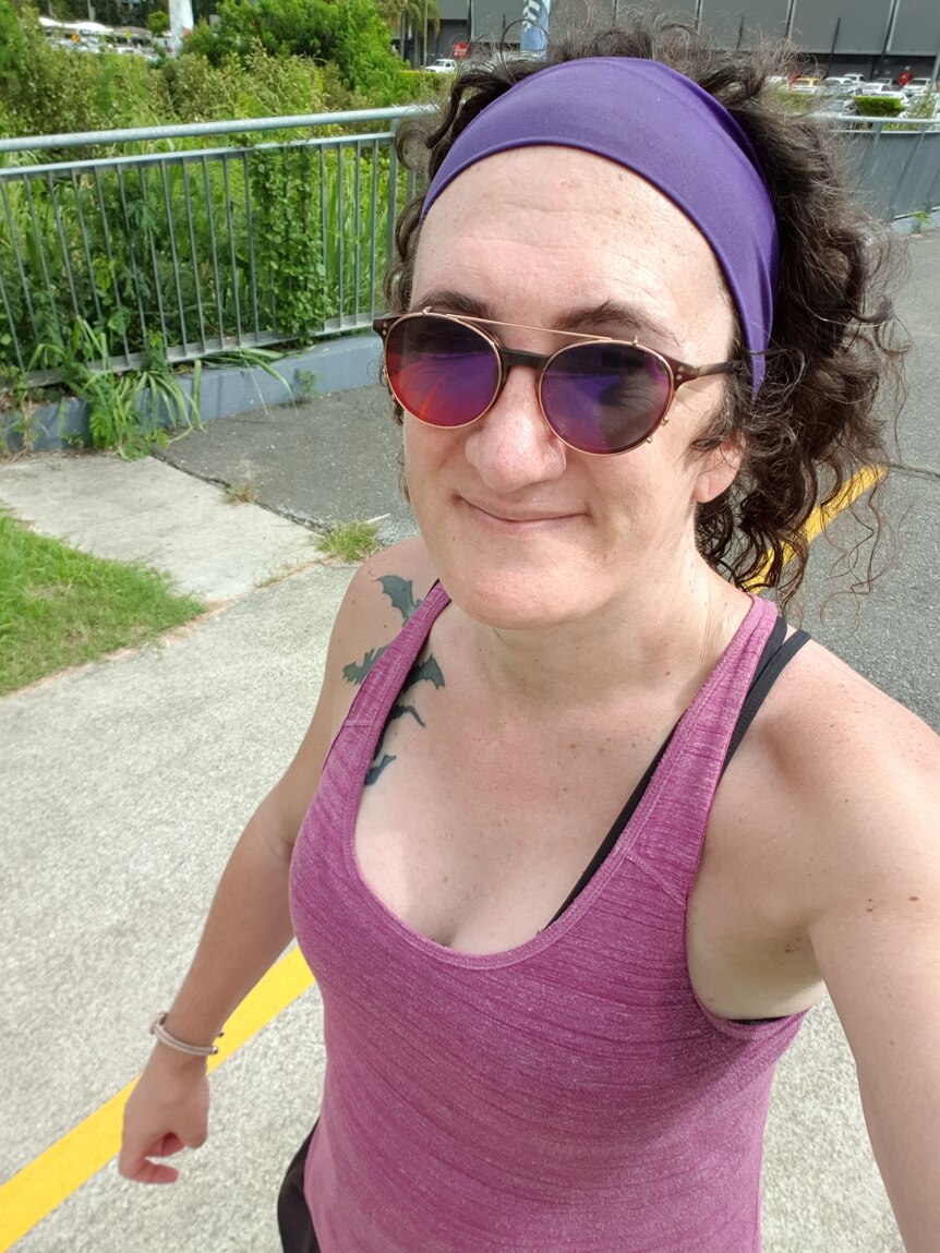 Ada takes a selfie at parkrun, they are wearing a pink singlet and sunglasses.