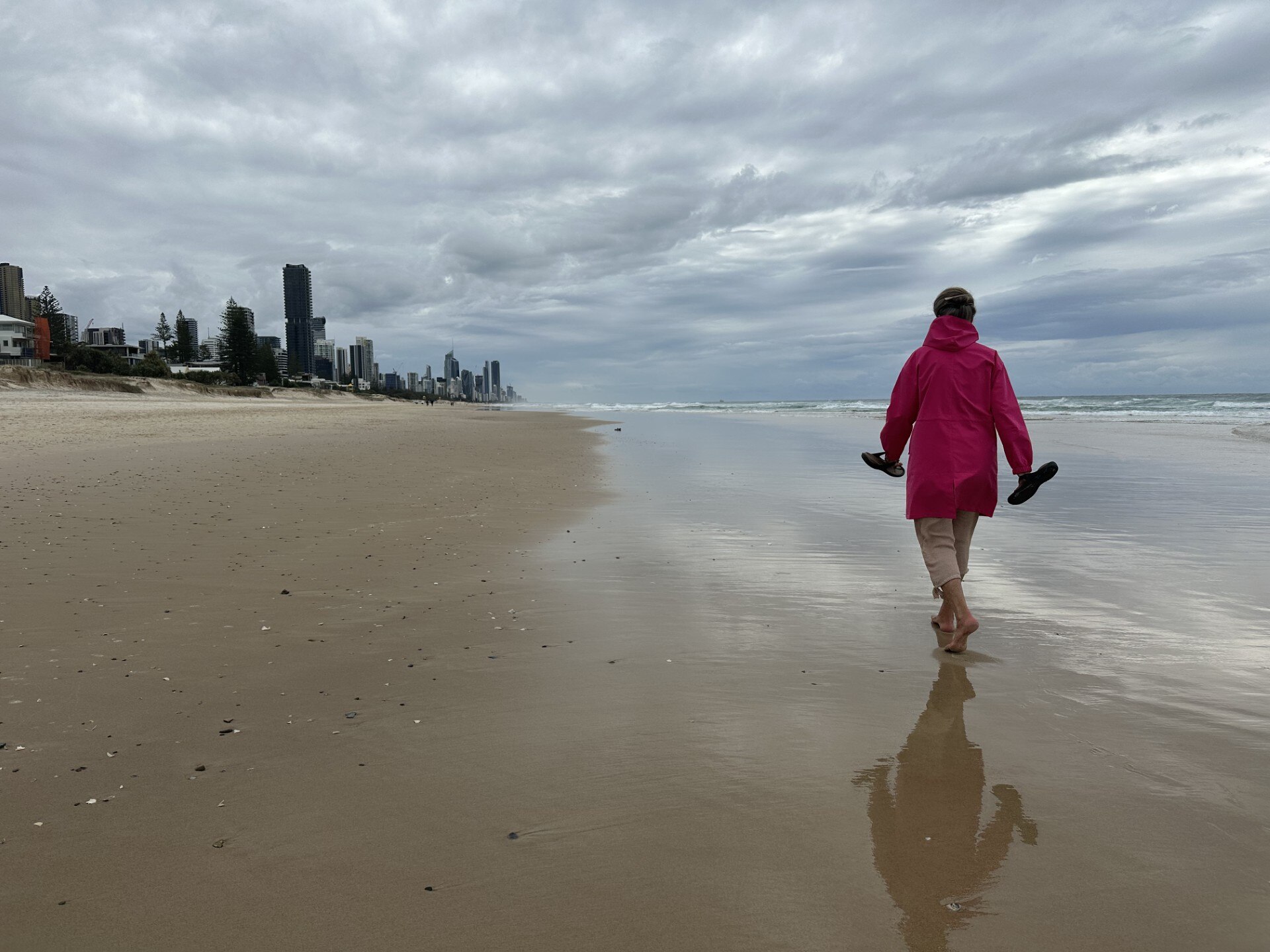 Woman in pink raincoat walking on beach.
