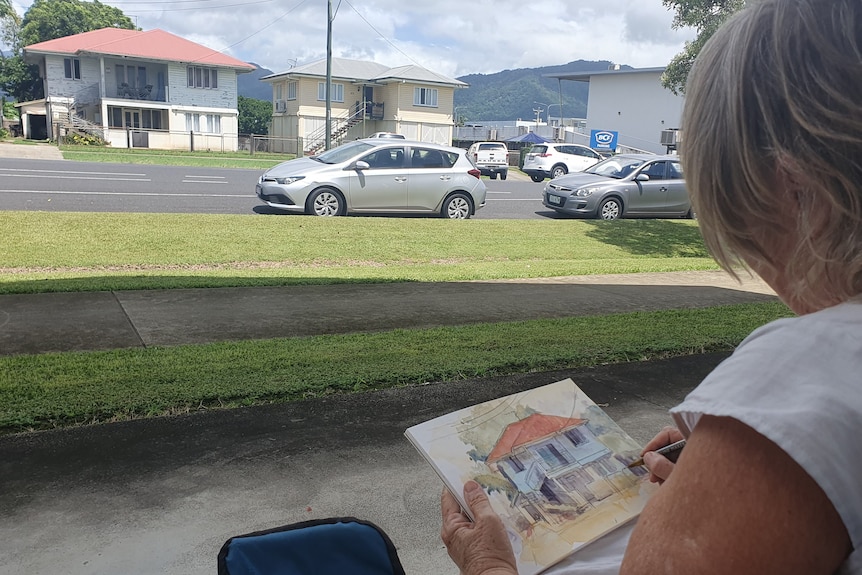 A woman sitting on a chair sketching while facing a suburban street.