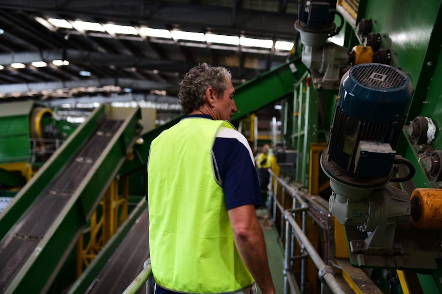 Man in high visual vest walks between machinery.