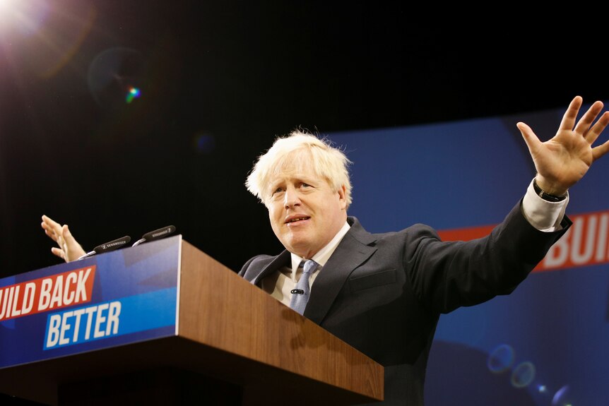 Boris Johnson gestures with his arms as his gives a speech in front of a lecturn.