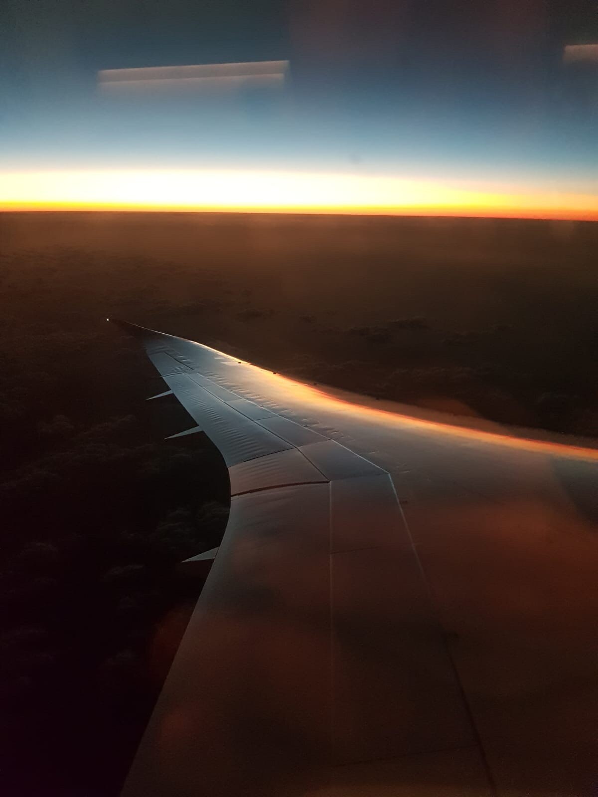 View of the wing of a plane and sunrise on the horizon.