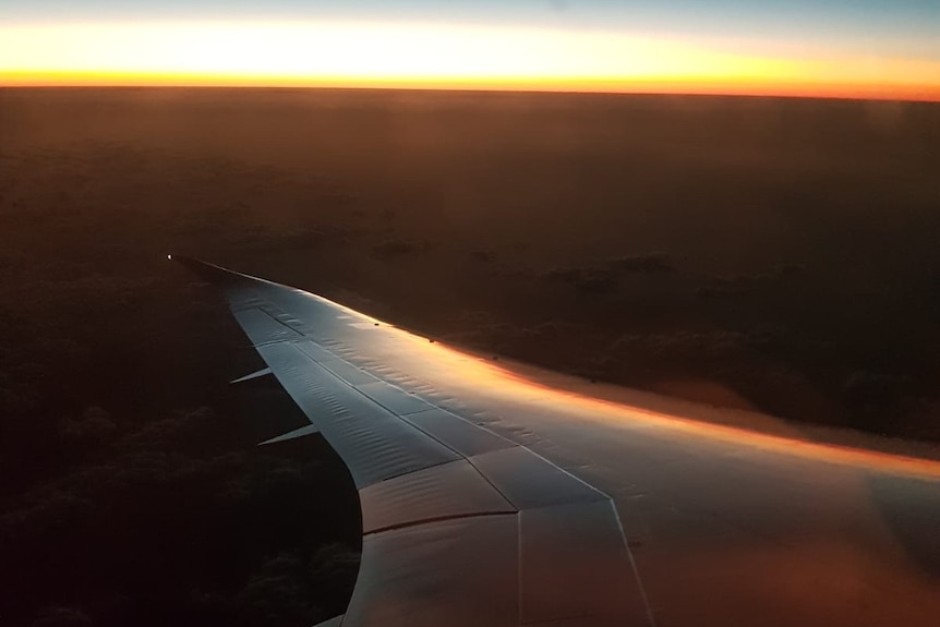 View of the wing of a plane and sunrise on the horizon.