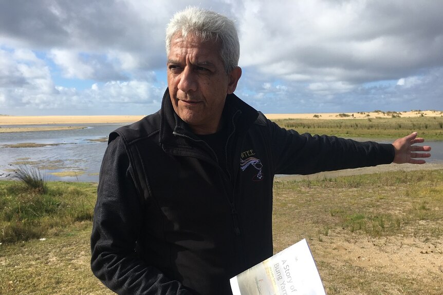 Indigenous man holding the book he wrote on the shoreline of Bung Yarnda