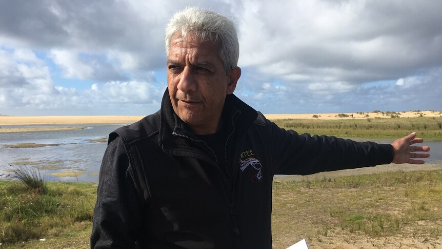 Indigenous man holding the book he wrote on the shoreline of Bung Yarnda.