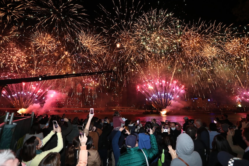 A crowd stands on the banks of the Brisbane River as fireworks go off.