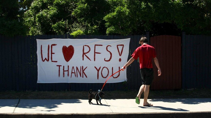 A man walks his dog past a sign thanking the Rural Fire Service.