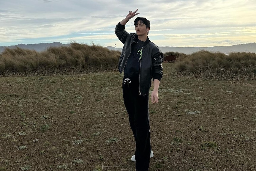 A man is standing near the beach doing a peace sign to the camera