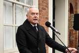Huw Edwards stands at a podium talking into a microphone