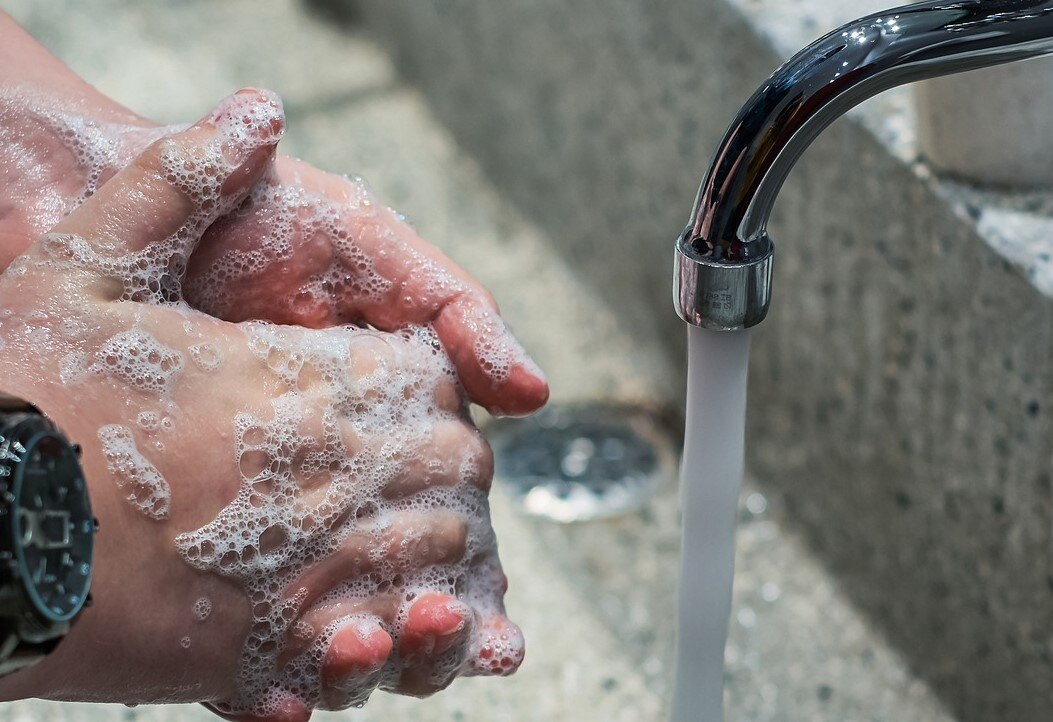 Close up of soapy hands near basin faucet that has water coming out.