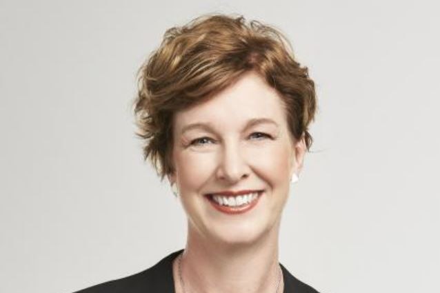 A headshot of a woman with short brown hair, wearing a black suit, smiling at the camera