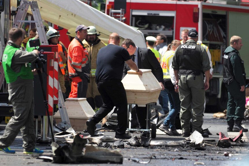 Undertakers and emergency services workers move wooden coffins at the site of a bus crash in Germany.