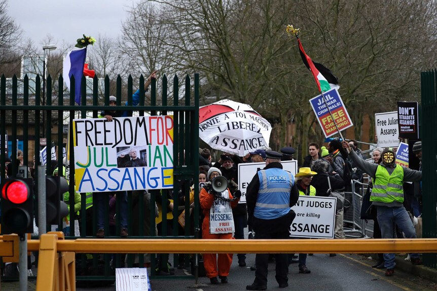 A policeman stands in front of protesters holding signs saying "freedom for Julian Assange".