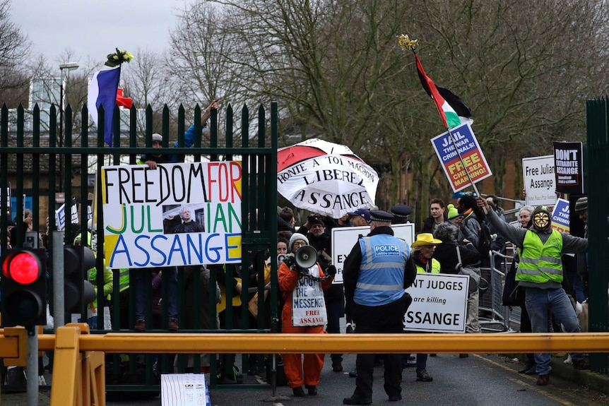 A policeman stands in front of protesters holding signs saying "freedom for Julian Assange".