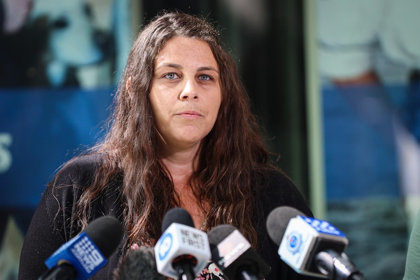 a woman with long brown hair speaking in front of the microphone