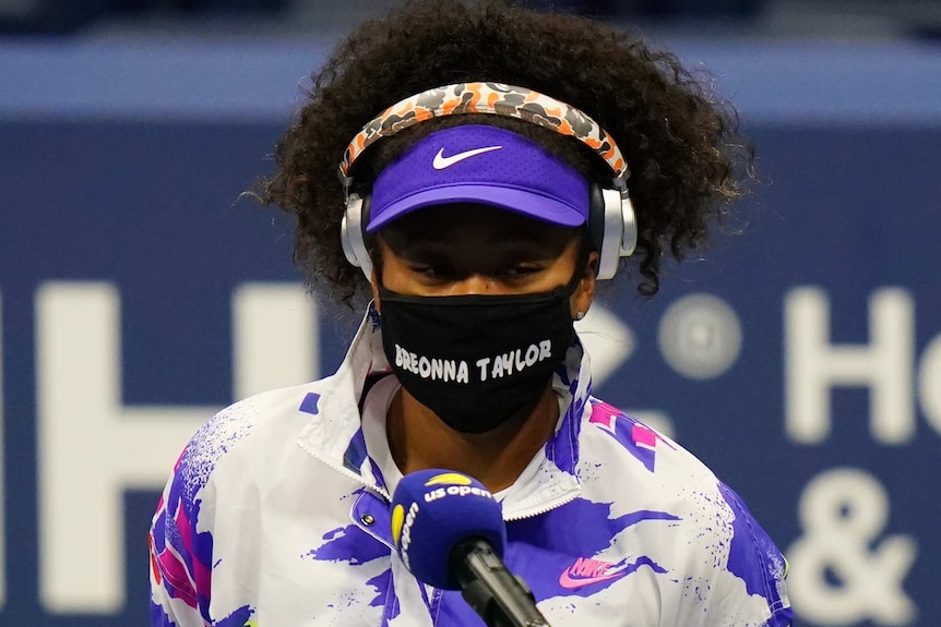 Naomi Osaka speaks into a US Open microphone while wearing a mask with Breonna Taylor written on it.