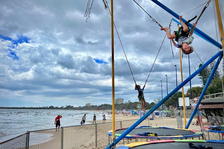 Trampolines on beach, with boy flipping upside down 