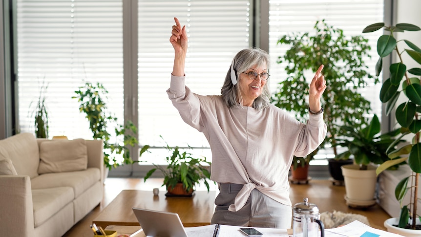 Woman with grey hair points her fingers while dancing in front of her laptop at home.