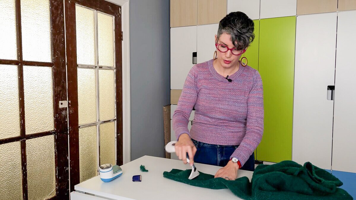 Erin Fitzgerald behind workbench, looking down at a jumper she is combing with de-pilling brush