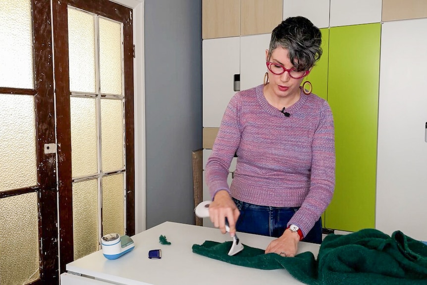 Erin Fitzgerald behind workbench, looking down at a jumper she is combing with de-pilling brush