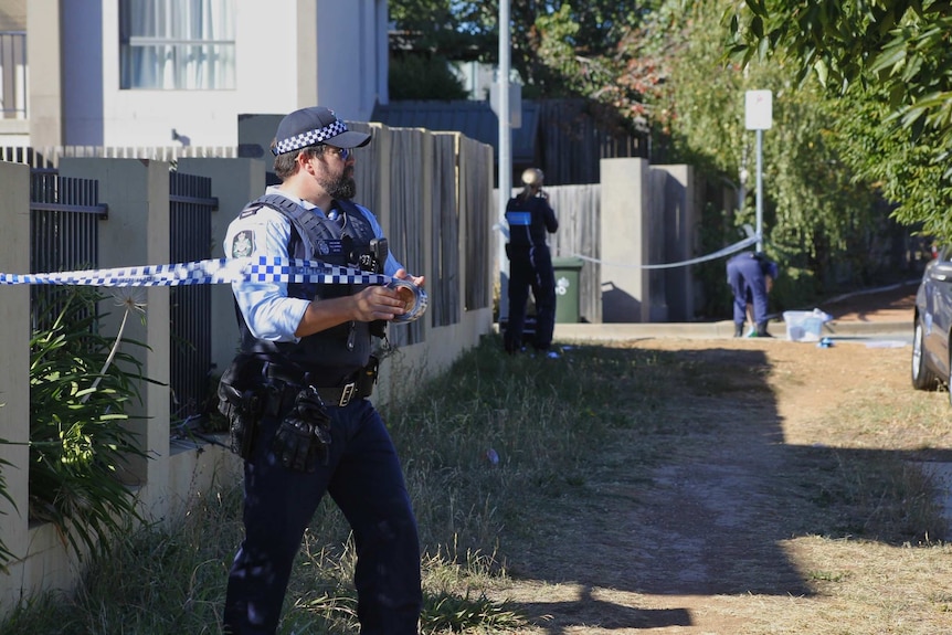 An officer reels out police tape at the crime scene.